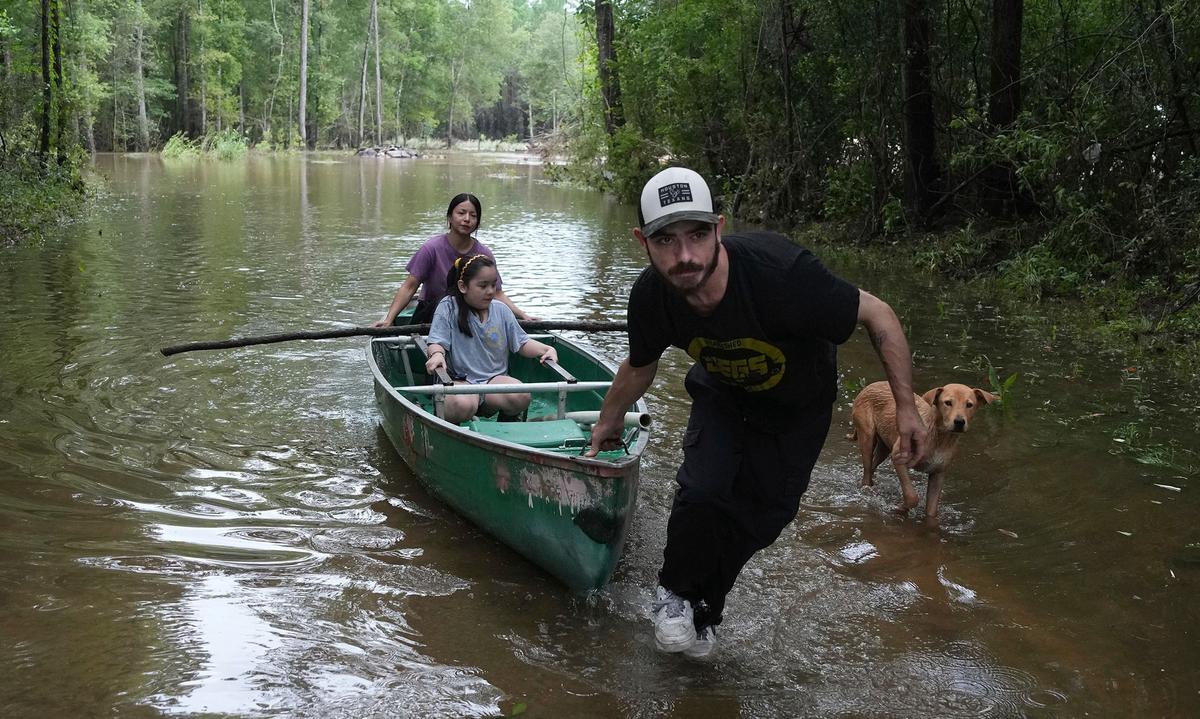 Man pulling canoe with daughter and dog nearby through floodwaters