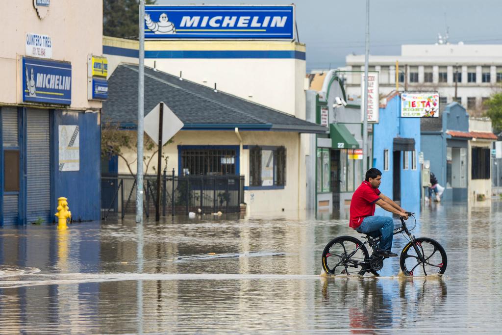 A man rides his bicycle through floodwaters in Watsonville, Calif., Saturday, March 11, 2023.