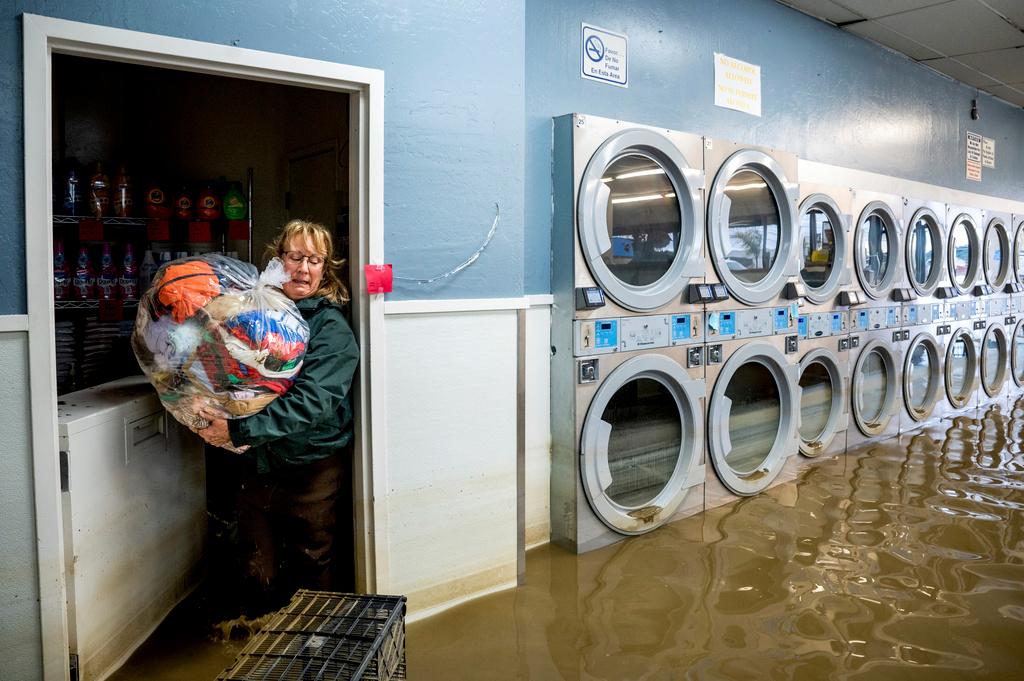 Pamela Cerruti carries clothing from Pajaro Coin Laundry as floodwaters surround machines in the community of Pajaro in Monterey County, Calif.