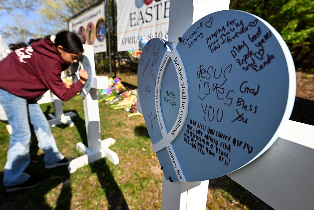 A youngster writes a message on crosses at an entry to Covenant School