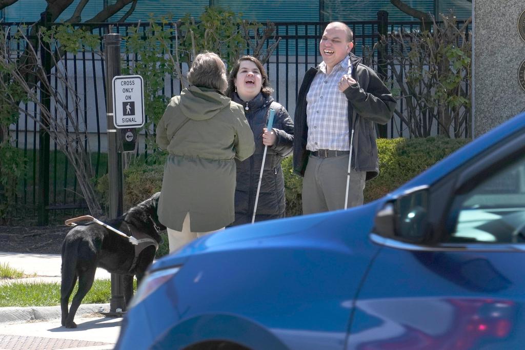 Maureen Reid, left, and her guide dog, Gaston, laughs with Sandy Murillo, center, and Geovanni Bahena, before they navigate Rosevelt Avenue, with audible signals for the blind in Chicago