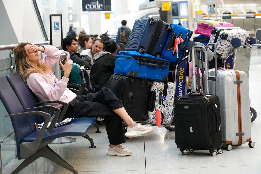 Passengers sit with their luggage in Terminal 1 at John F. Kennedy International Airport in New York, Friday, Feb. 17, 2023. A power outage in the terminal has stretched into a second day. The outage has stranded passengers and forced flights to be canceled or diverted to other airports. 