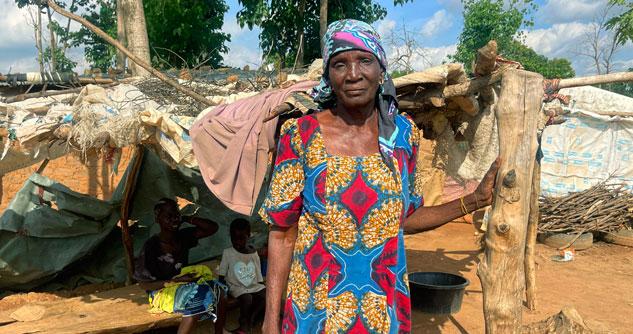 Woman standing in front of a makeshift shelter with children in the background