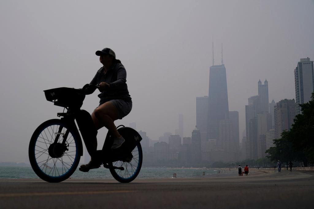 A person rides a bicycle along the shore of Lake Michigan as the downtown Chicago skyline is blanketed in haze from Canadian wildfires