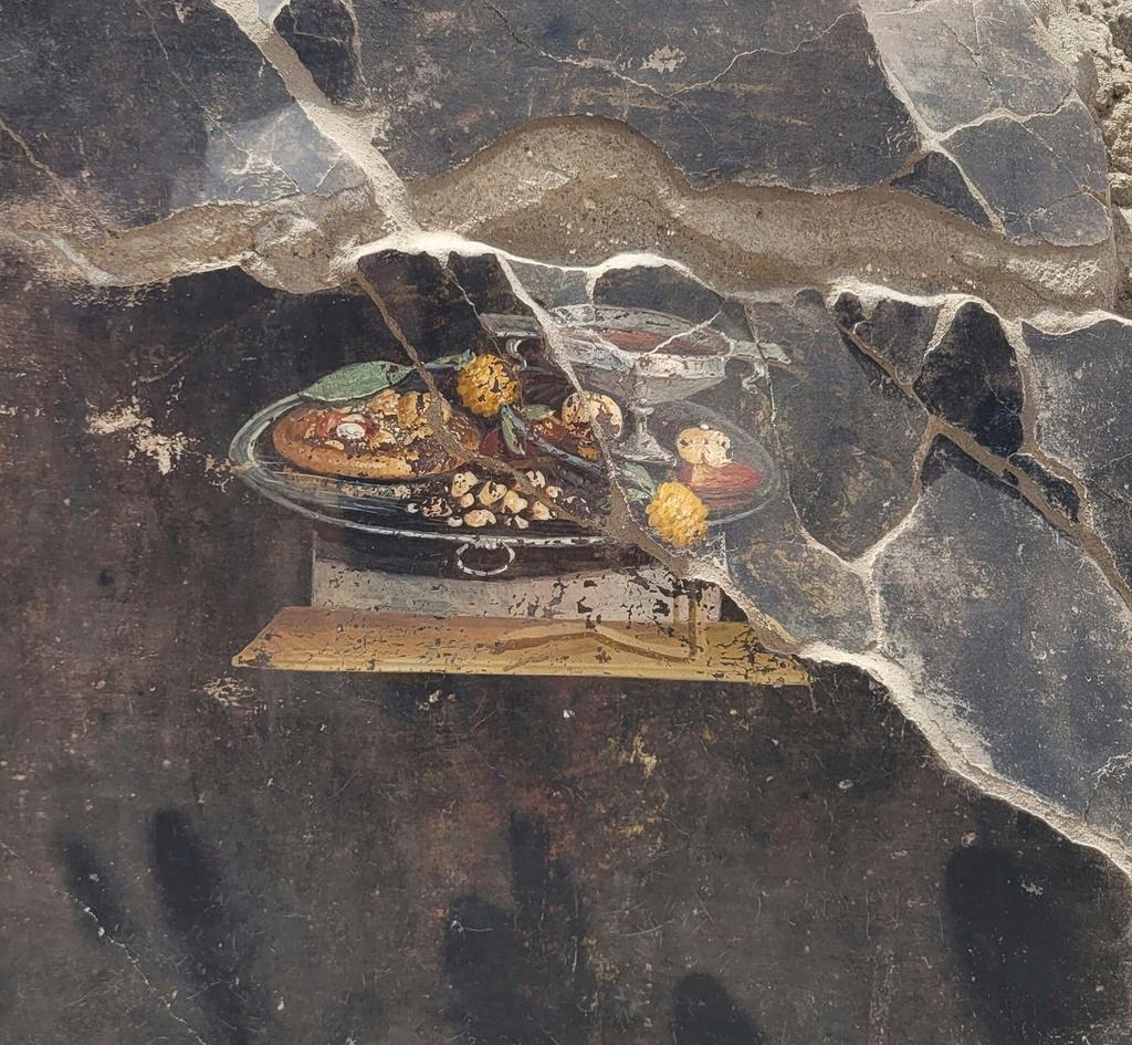 The wall of an ancient Pompeian house with a fresco depicting a table with food