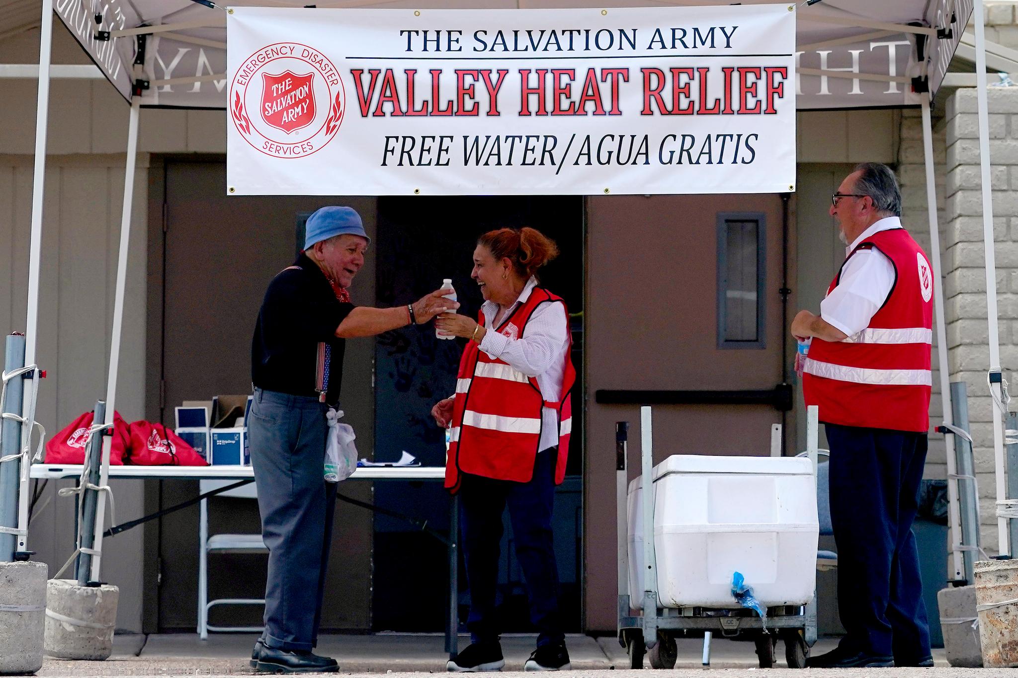 Salvation Army volunteer Francisca Corral, center, gives water to a man at a their Valley Heat Relief Station, Tuesday, July 11, 2023 in Phoenix.