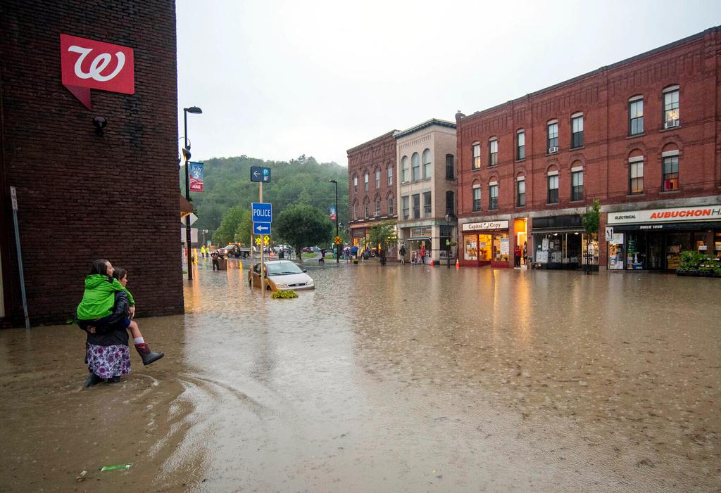 Pedestrians navigate floodwaters outside City Hall, Monday, July 10, 2023, in downtown Montpelier, Vt.