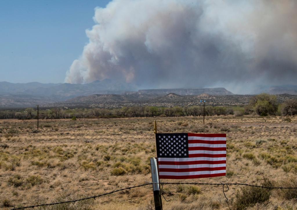 An American Flag on a fence blows in the wind along NM 22 as the Cerro Pelado Fire burns in the Jemez Mountains, April 29, 2022, in Cochiti, N.M. 