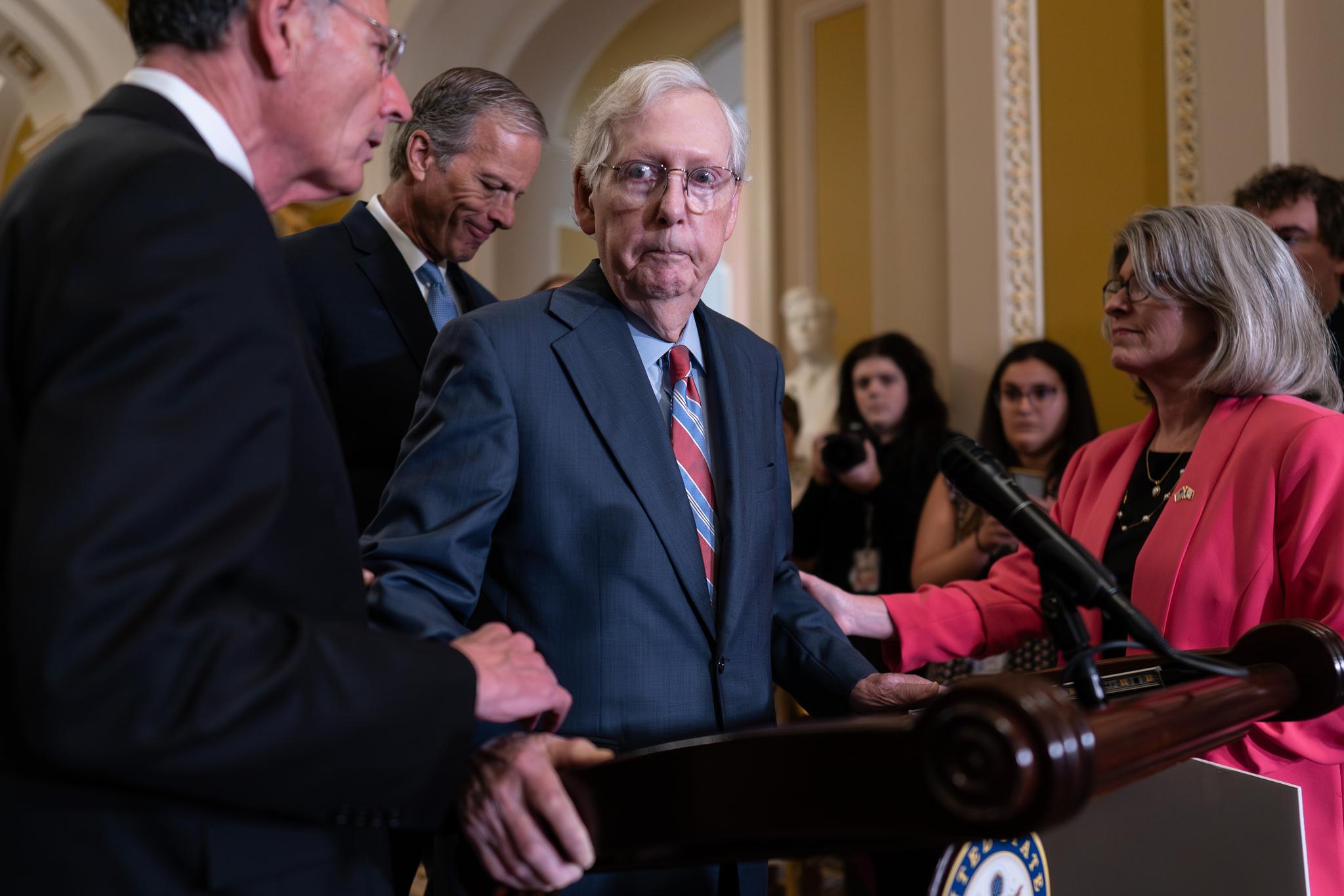 Mitch McConnell being held by the arms by several senators