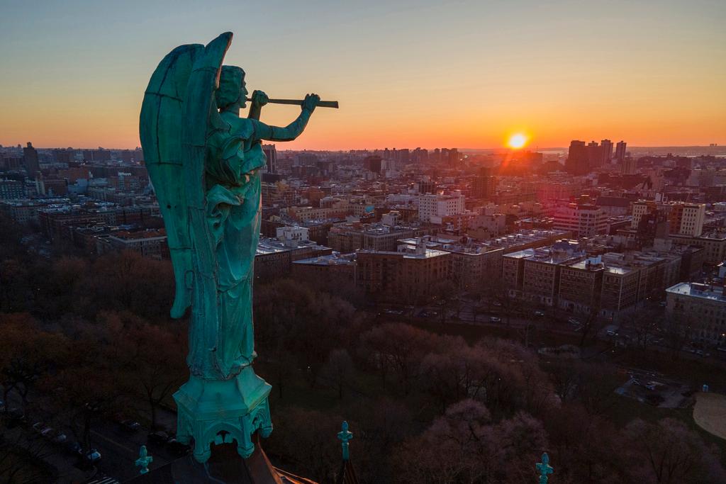 A bronze statue of the Archangel Gabriel blowing a trumpet stands at the Cathedral of St. John the Divine as the sun rises in the Morningside Heights neighborhood of the borough of Manhattan in New York 