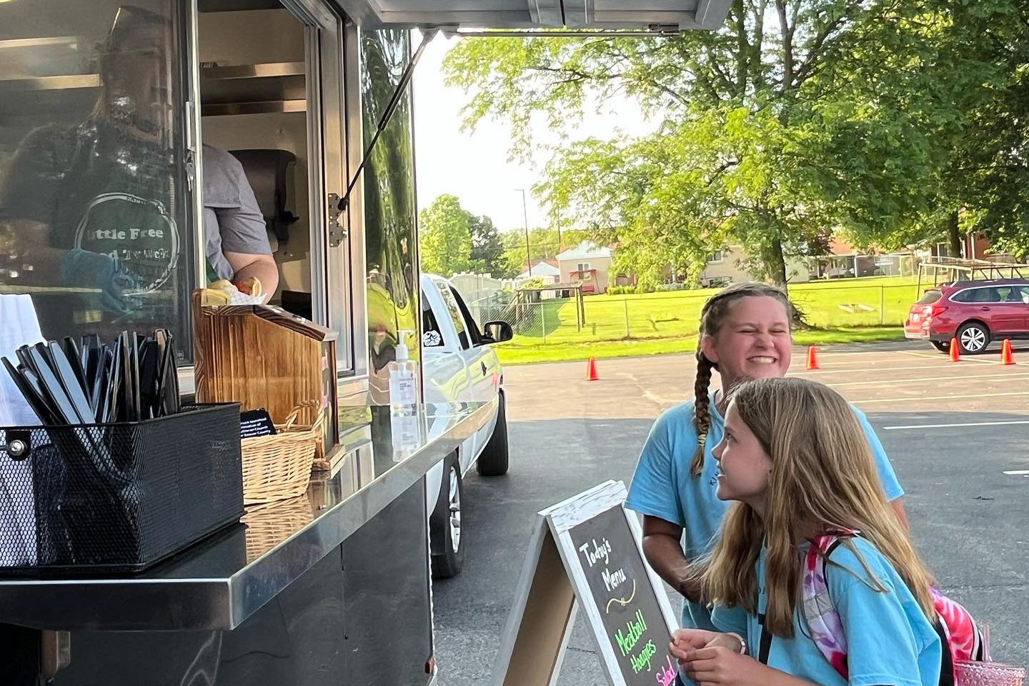 Two school-aged children walking up to the Little Free Food Truck, smiling