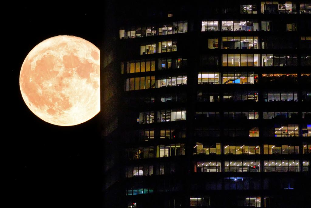 The full moon passes behind the illuminated windows of a New York City skyscraper