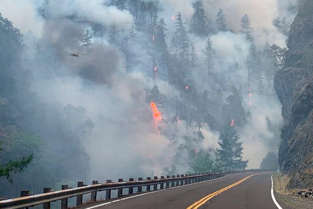 Smoke and flames rise from the Smith River Complex Fire next to the closed U.S. Route 199 in Gasquet, California