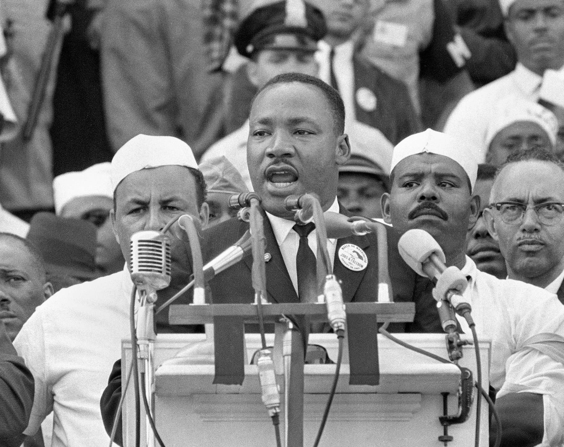 Rev. Dr. Martin Luther King, Jr. with lots of people behind him, in front of multiple microphones