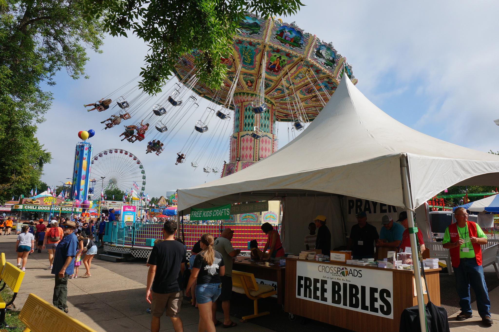 State fair with a tent and a sign saying "Free Bibles"