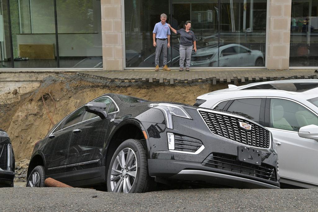 From left, car dealership owner Rick Durand Owner of Durand Cadillac and controller Michelle Bettez react beside three vehicles that fell into a sinkhole that was washed out of his car dealership