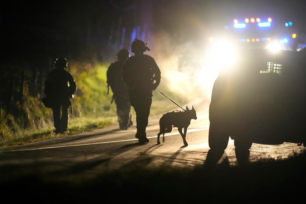 Law enforcement walks with a police dog outside a property on Meadow Road in Bowdoin, Maine