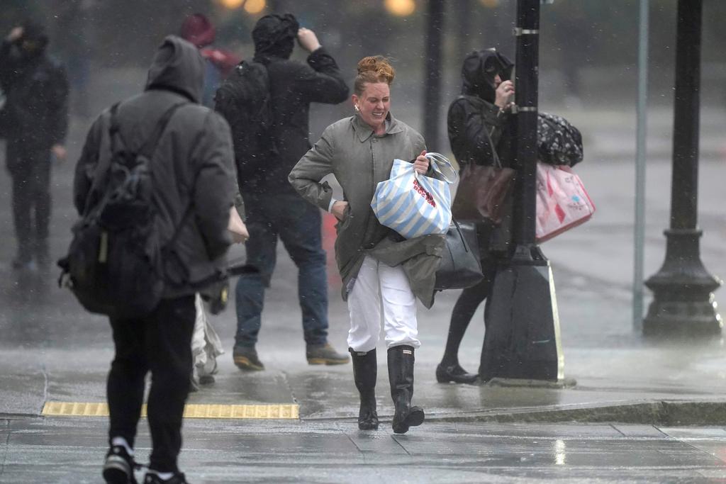 Pedestrians are buffeted by wind and rain as they cross a street in Boston