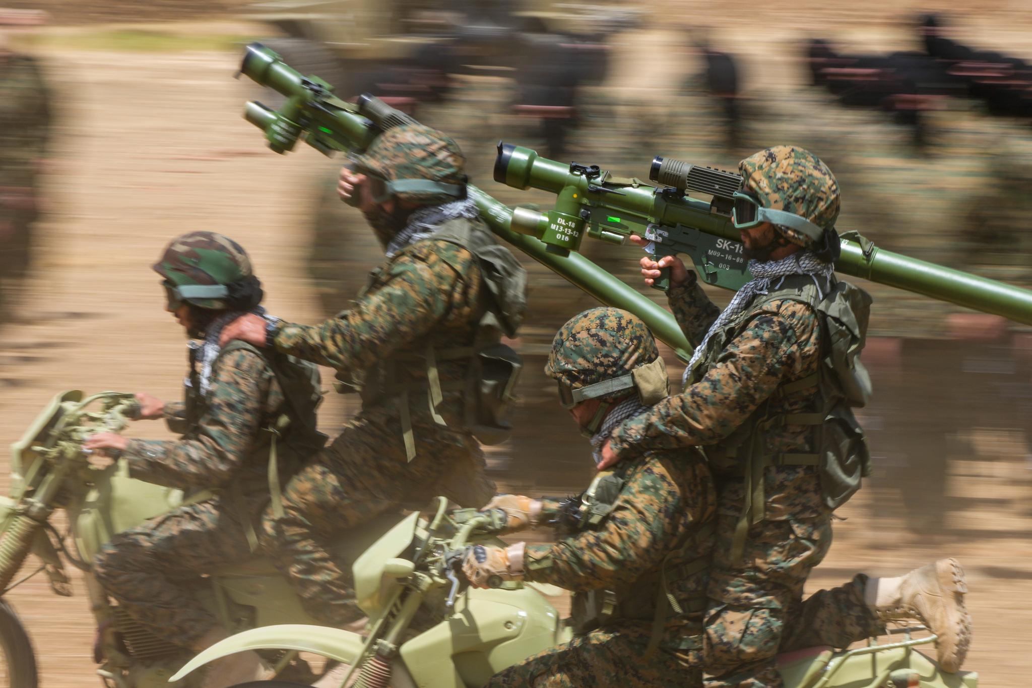 Men in camo, holding rocket launchers on the back of dirt bikes