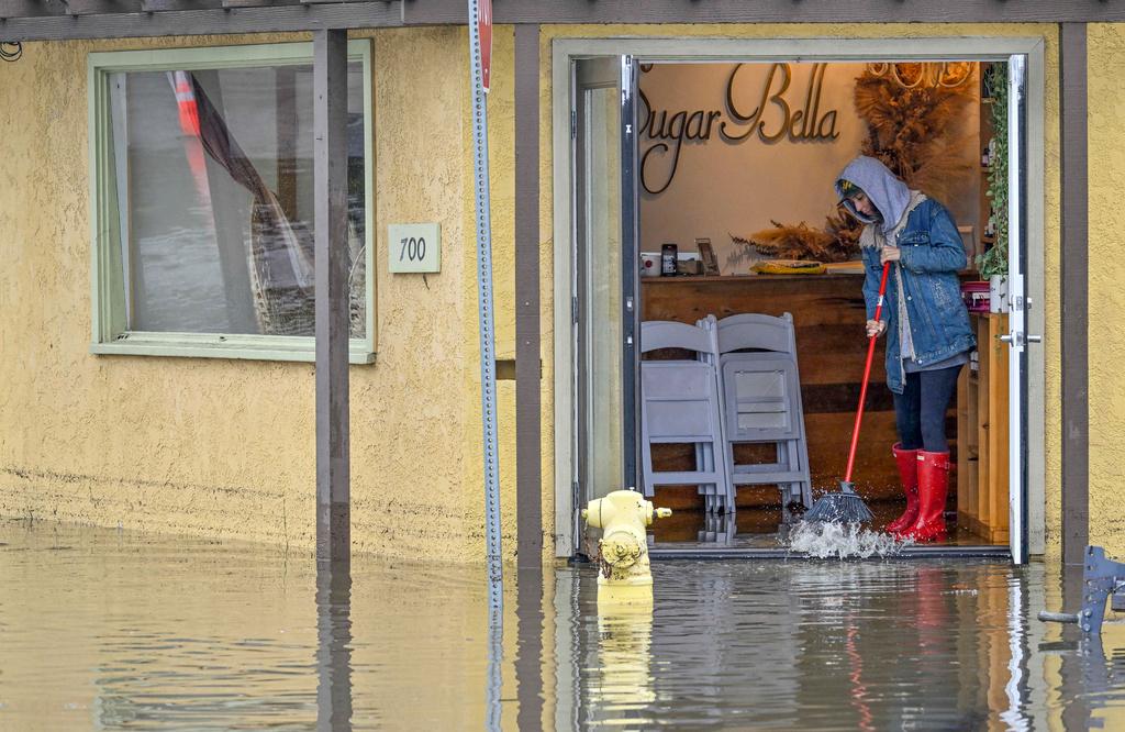 A worker at Sugar Bella sweeps flood waters out the front door on Marina Drive, just south of Pacific Coast Highway