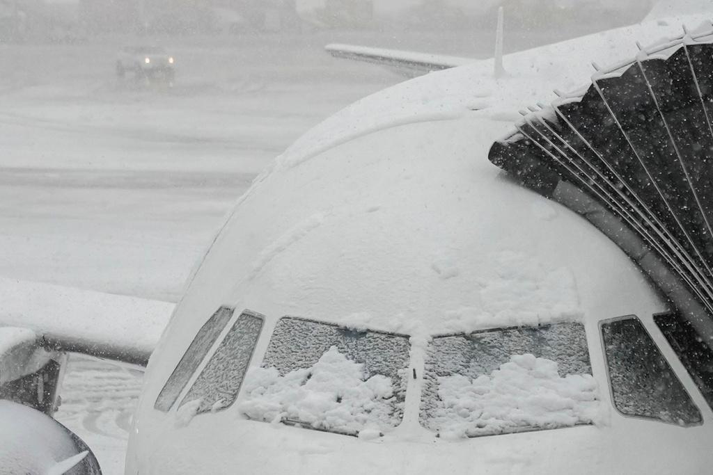 Snow covers the windows of a plane that sits at a gate at John F. Kennedy International Airport