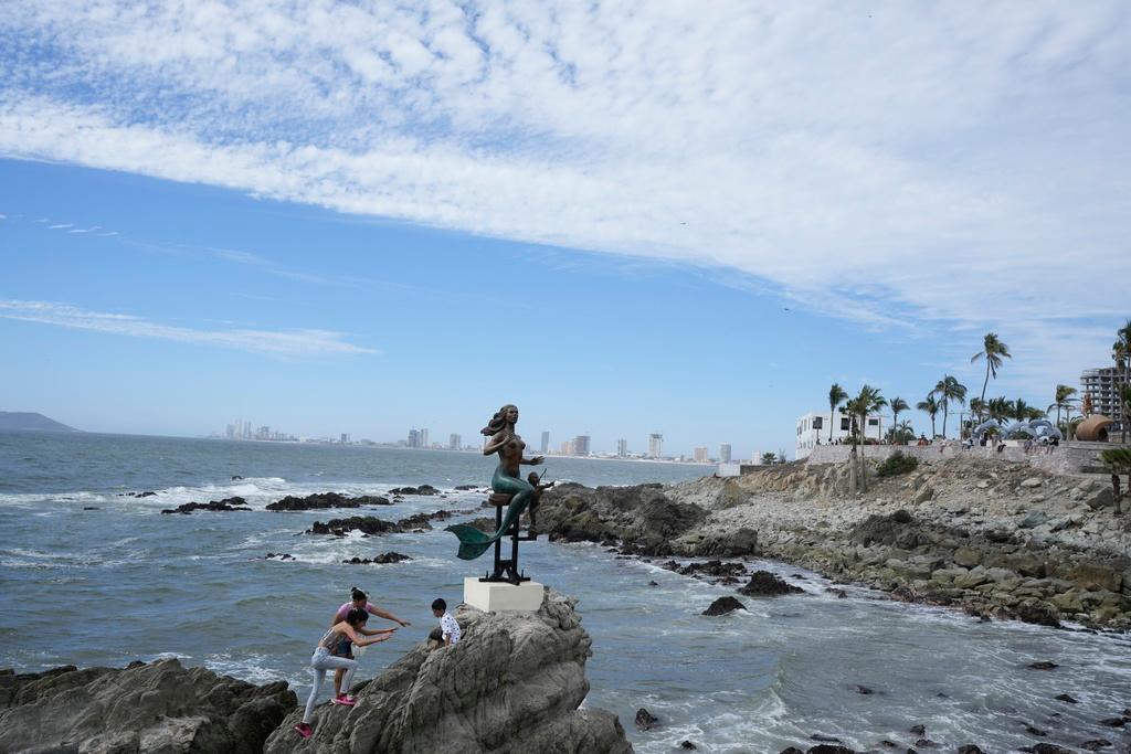 Tourists climb a mermaid statue the day before a total solar eclipse in Mazatlan, Mexico