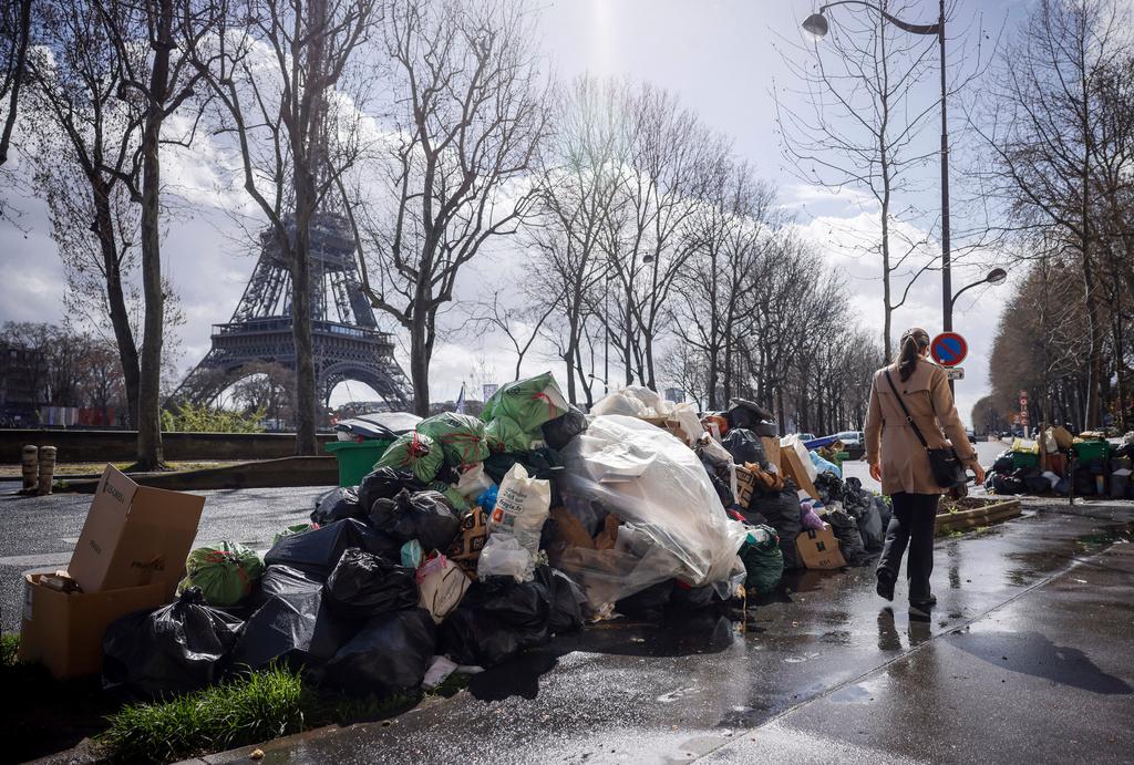 A woman walks past a pile of uncollected garbage near Eiffel Tower in Paris, Friday, March 24, 2023.