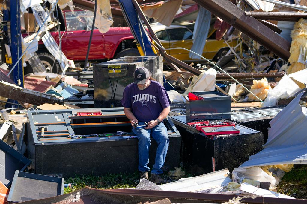 An employee of a body shop collects tools from damage after a tornado rolled through Valley View, Texas