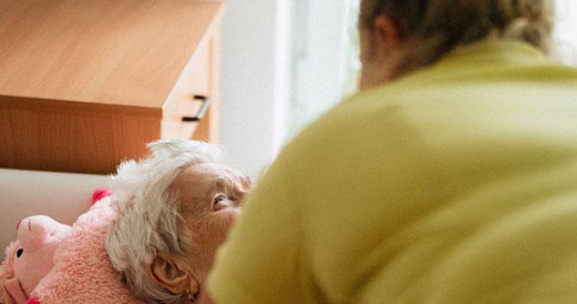 Woman in yellow shirt assists elderly woman lying down