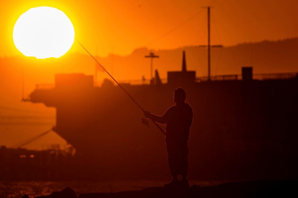 A man fishes off a jetty in Alameda, Calif., as the sun sets over the San Francisco Bay 