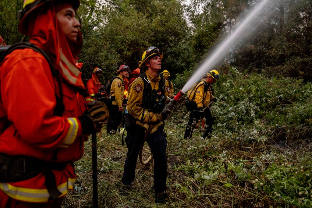 Rocco Olhiser, a firefighter with the Colusa Fire Department, center, douses water on a burning tree while battling the Thompson fire in Oroville, Calif.