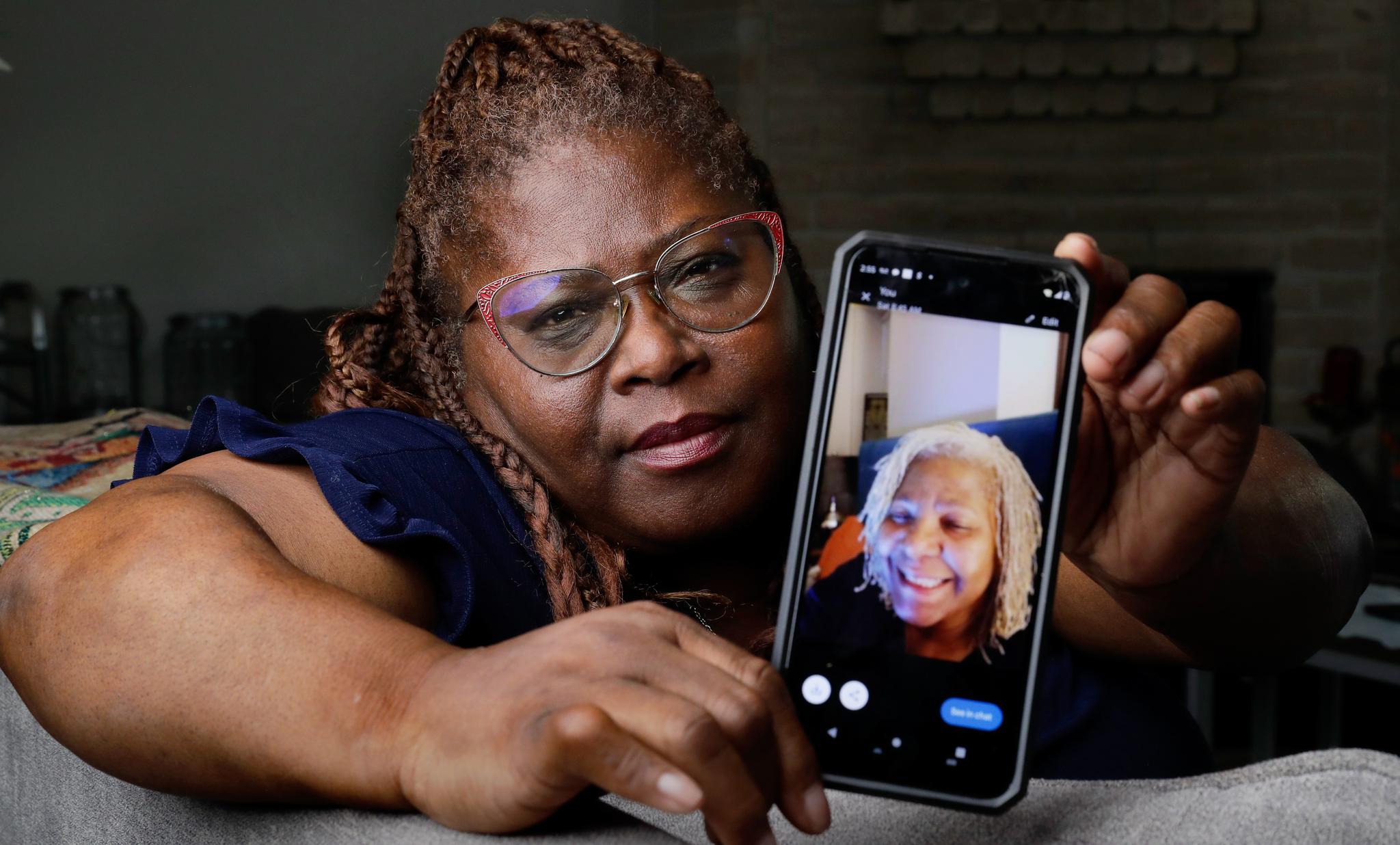 Woman with glasses holding a phone with a picture of her sister