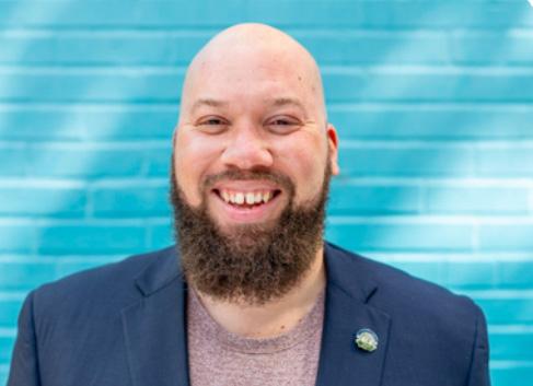 Man smiling in front of a teal wall