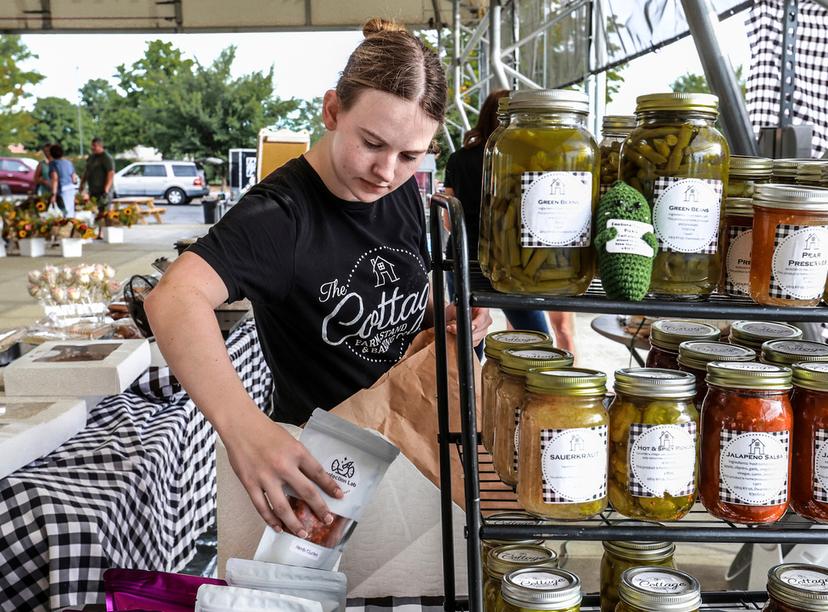 Lexia Smith stocks product while working in The Cottage Farm Stand & Baking Co. vendor booth set up at the Owensboro Regional Farmers' Market in Owensboro, Ky