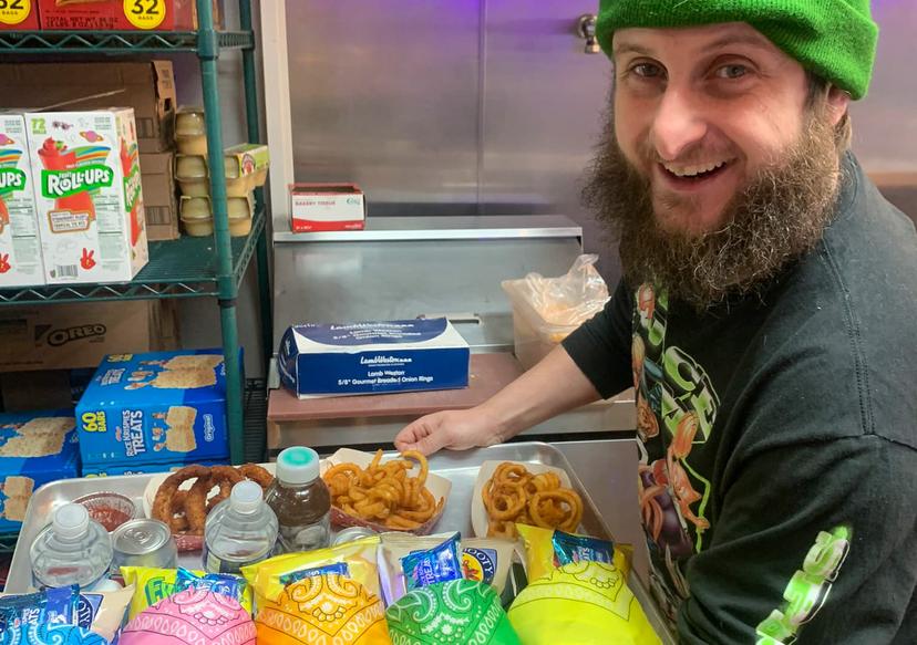 Man with green hat serving burgers and onion rings. Burgers have bandanas on them