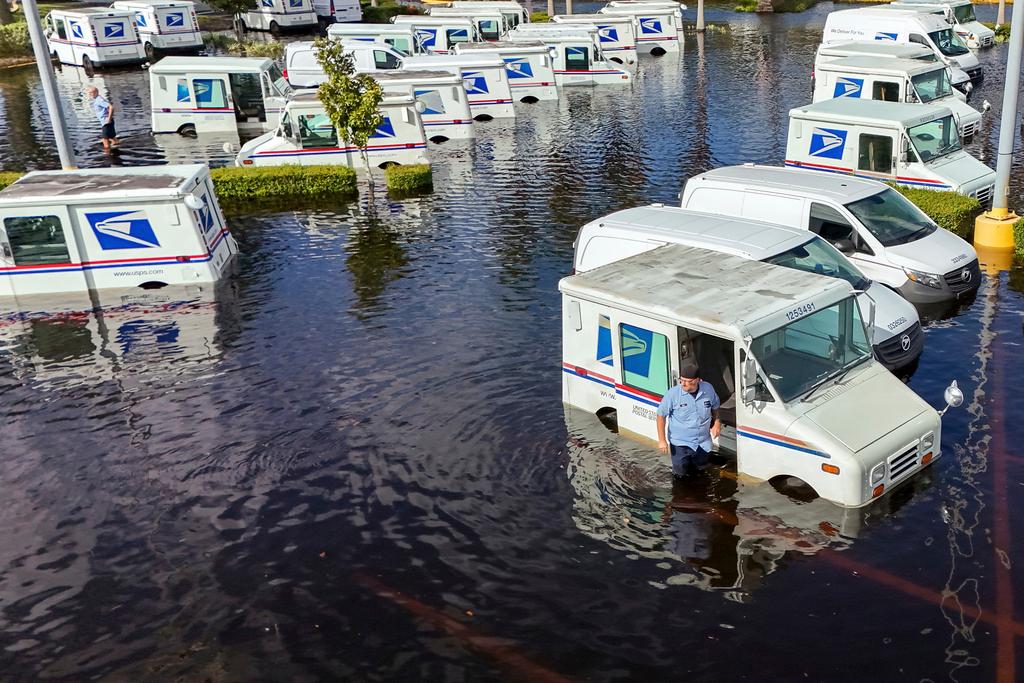 USPS worker inspects trucks that had been relocated to protect them from wind but which are now underwater as intense rain from Hurricane Milton caused the Anclote River to flood