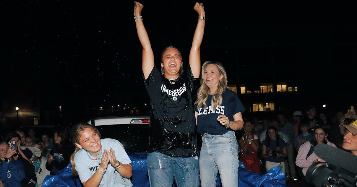 Woman has fists raised in the air as two other women cheer her on, in the back of a pickup