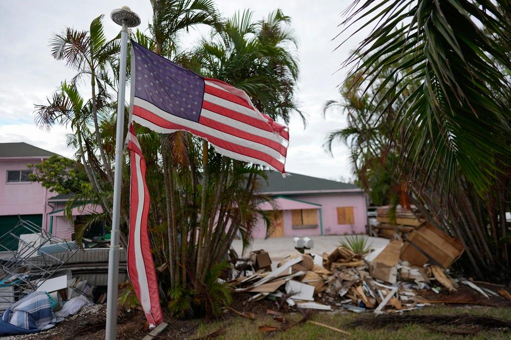 FILE - A tattered American flag flaps outside a home as furniture and household items damaged by Hurricane Helene flooding sit piled along the street awaiting pickup, ahead of the arrival of Hurricane Milton, in Holmes Beach on Anna Maria Island, Fla., Tuesday, Oct. 8, 2024. 