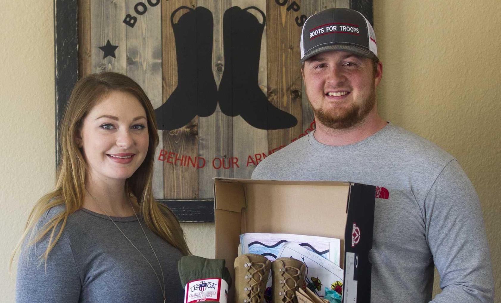 Wife and husband smiling and holding a box of combat boots and other items for a care package