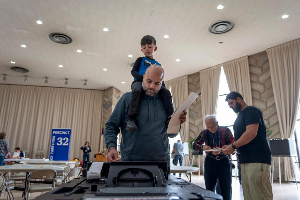 Three-year-old Zayn, sits on his father's shoulders as he inserts his ballot into a machine to vote at the First Presbyterian Church of Dearborn, Mich.