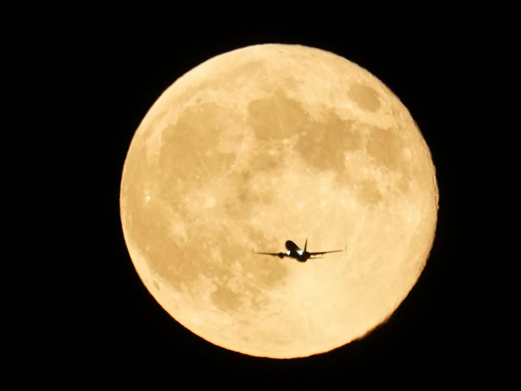 Airplane flies past the moon as it rises over Lake Michigan