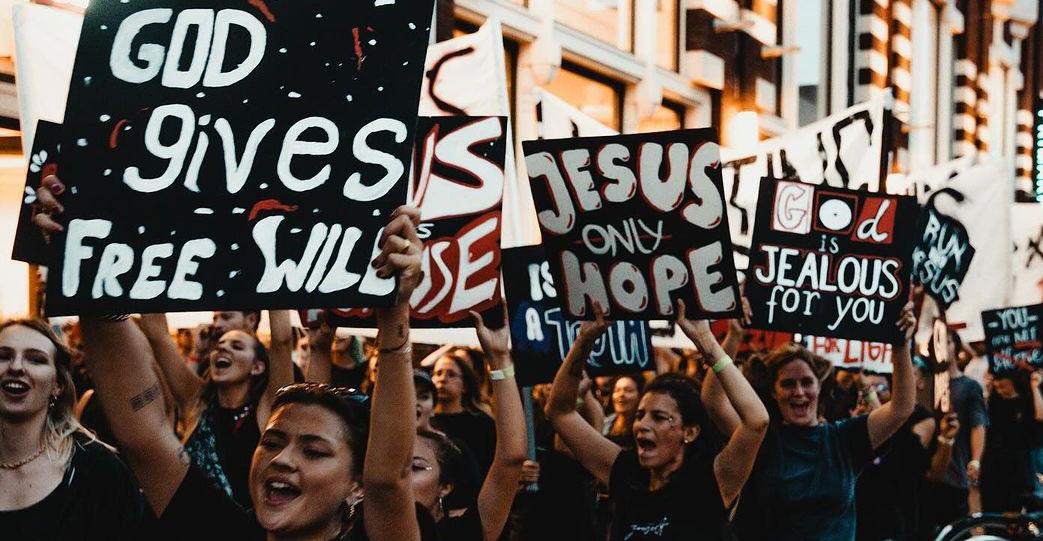 Young people with signs that say things like "God Gives Free Will" "Jesus Only Hope" and "God is jealous for you"