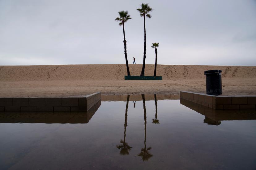 A person walks along the beach with flooding along the boardwalk Thursday, Feb. 1, 2024 in Seal Beach, Calif. 