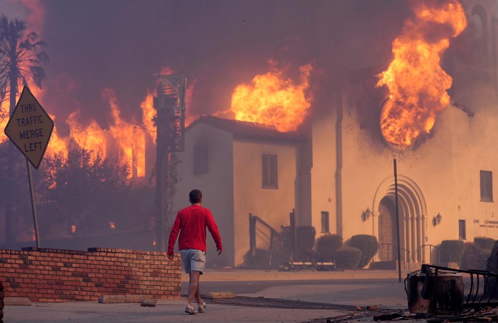 Man walks in front of the burning Altadena Community Church in the downtown Altadena section of Pasadena, Calif.