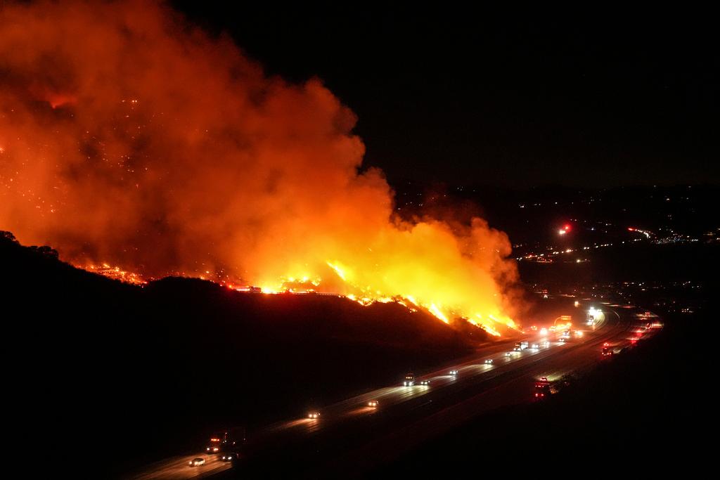 Vehicles drive along Interstate 15 as the Lilac Fire burns along a hillside in Bonsall, Calif.