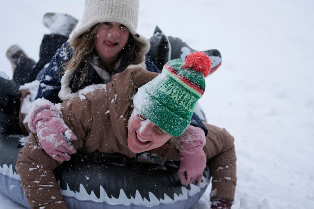 Abbie Schuh and her 8-year-old daughter Louise Delisio get covered in snow as they sled down a hill at Herman Park in Houston