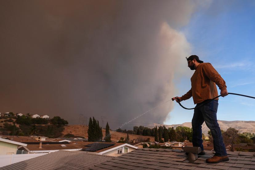 Andrew Aguilar sprays water from the top of the roof at his brother's home Castaic, Calif.,