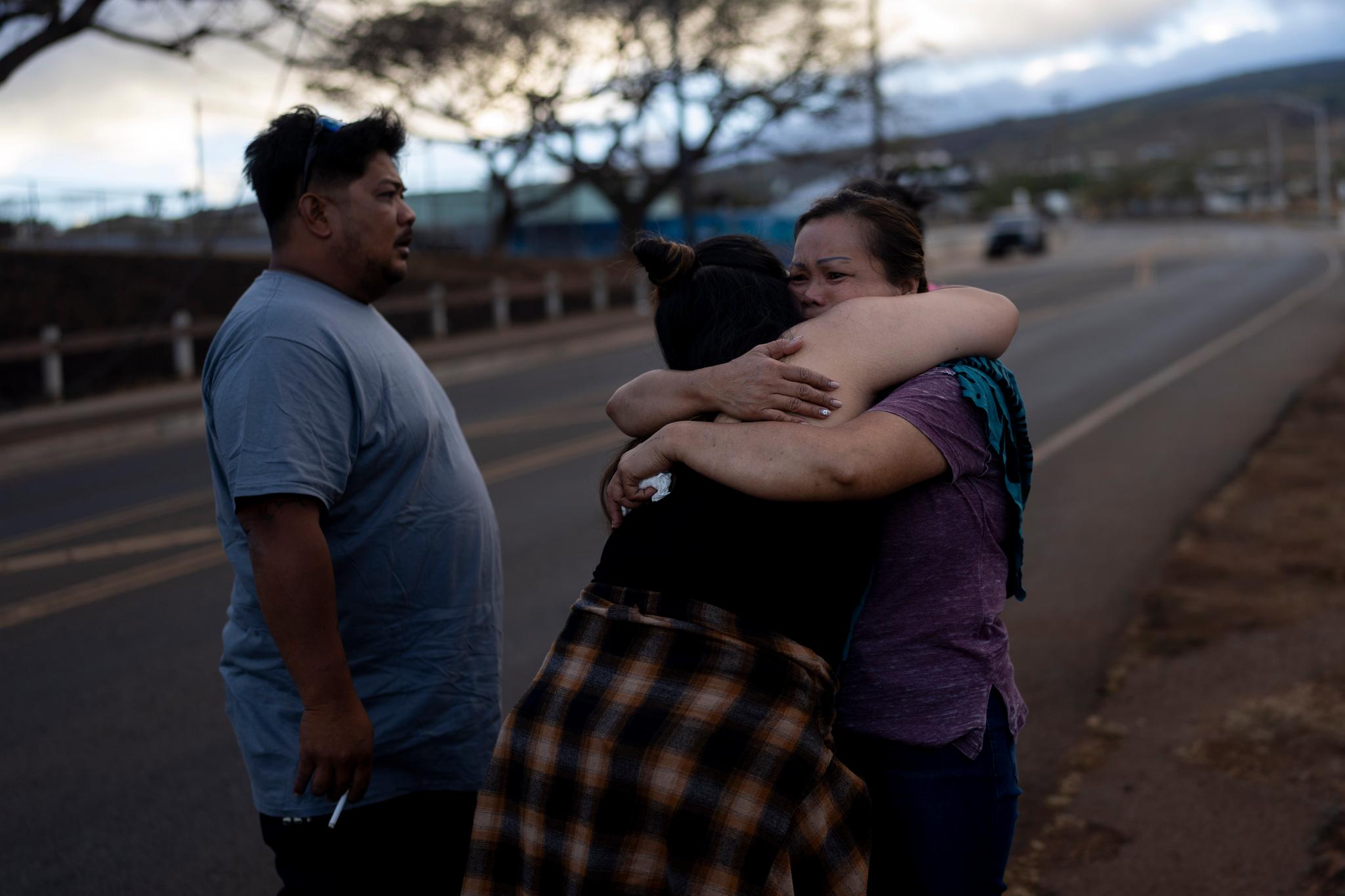 A man stands back as two women hug.