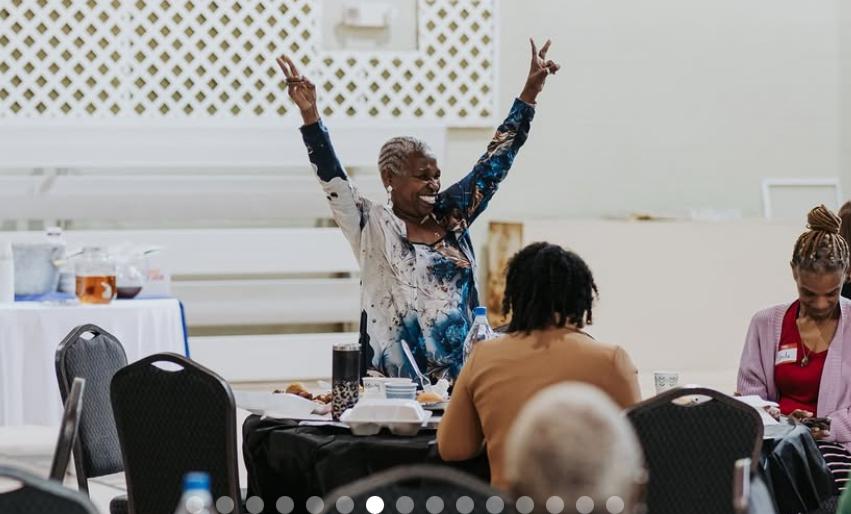 Woman standing in front of other women with her hands up with a big smile on her face