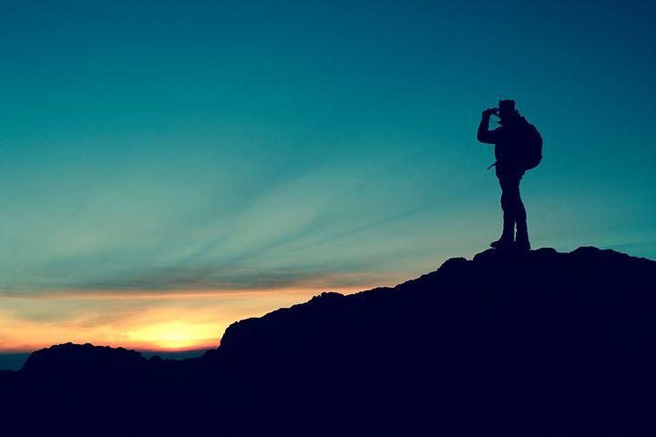 Silhouette sunset image of hiker standing in top of small hill